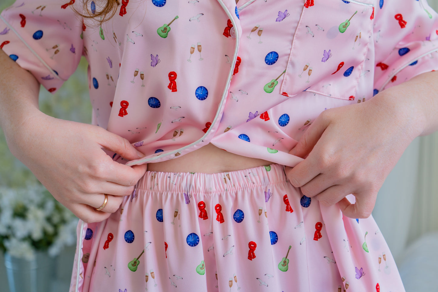 A close-up of satin pajamas with fun, detailed icons: guitars, vinyls, clocks, paying tribute to Midnights and its dreamy late-night aesthetic.